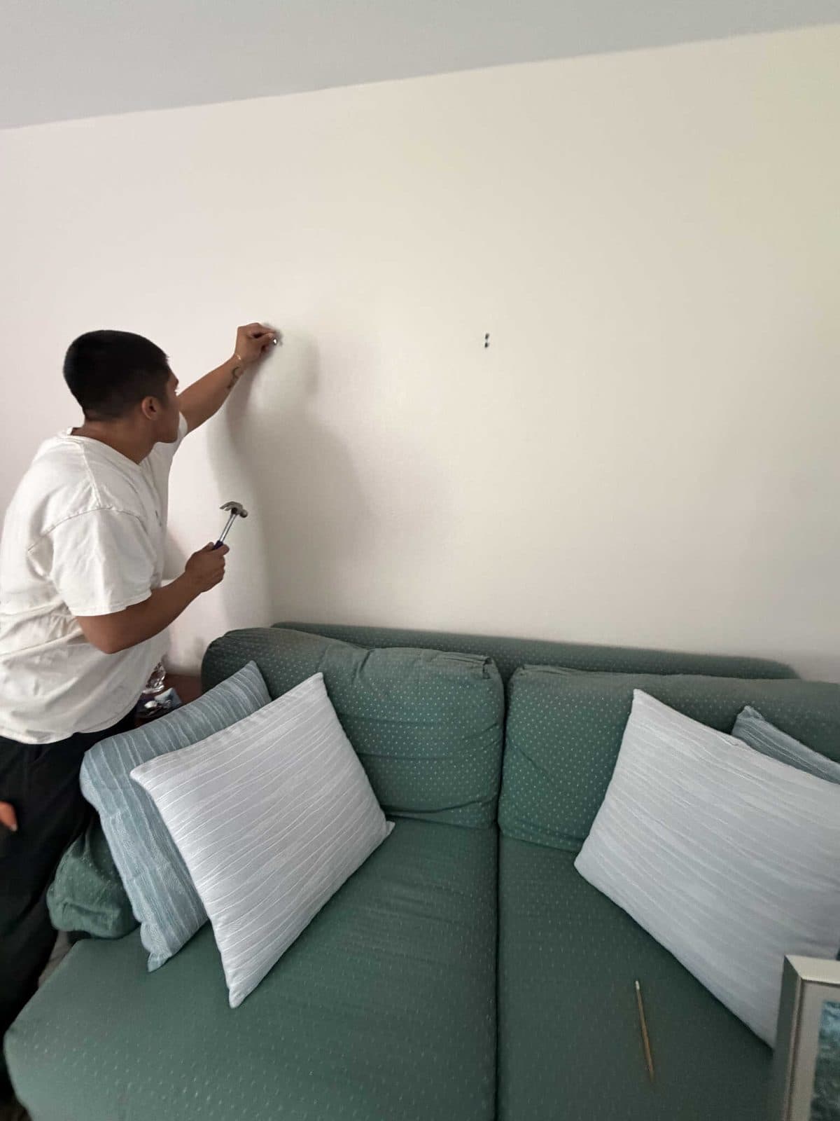Student Bee Ben hanging a picture in a client's living room